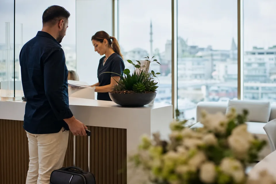 A patient with a small suitcase is welcomed at a modern clinic reception on the day of his procedure